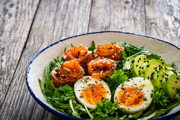 Salmon salad - smoked salmon, hard boiled eggs, avocado and leafy greens on wooden table
