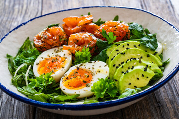 Salmon salad - smoked salmon, hard boiled eggs, avocado and leafy greens on wooden table
