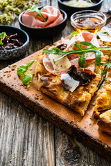 Pinsa Romana with mortadella, parmesan cheese and vegetables on wooden table
