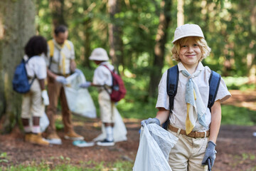Waist up portrait of cute boy scout helping clean forest and smiling at camera, copy space
