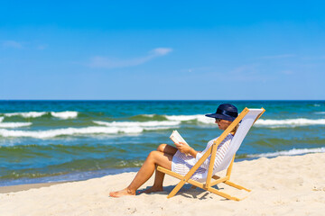 Fototapeta premium Woman relaxing on beach reading book sitting on sunbed 