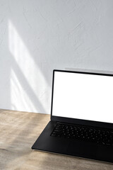 laptop with blank screen mockup on beige wooden table, aesthetic sunlight shadows on white wall,...