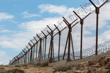 A fence with barbed wire. A long wire fence with barbed wire. Protection of borders and military territories