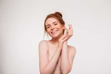 Beautiful young happy fresh redhead model girl with a cute smile and clean skin applies cream on her hands and does skin care on a white background. Beauty and health