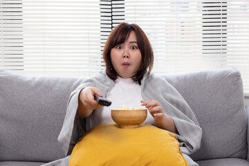 Plump Asian Woman with Shocking Face Watching Excited Television Show While Eating Popcorn on the Couch