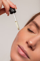 Beautiful young fresh girl drips cosmetic oil from an eyedropper on her facial skin, closeup. Beauty and skin care