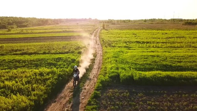 a motorcyclist in gear rides on a dirt road through a field