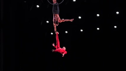 Circus aerial hoop duo with on black stage background performing trick, highly risky drop. Concept of trust and confidence