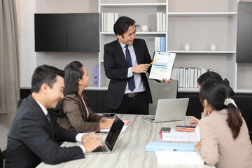 Collaborative process of young asian business people team working together discussing, researching, brainstorming and planning work at business meeting in modern office building and city background