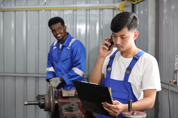 Multiethnic technicain mechanic using metal lathe machine operate polishing car disc brake with smart mobile phone and clipboard at garage. Maintenance automotive and inspecting vehicle part concept