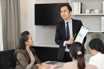 Collaborative process of young asian business people team working together discussing, researching, brainstorming and planning work at business meeting in modern office building and city background
