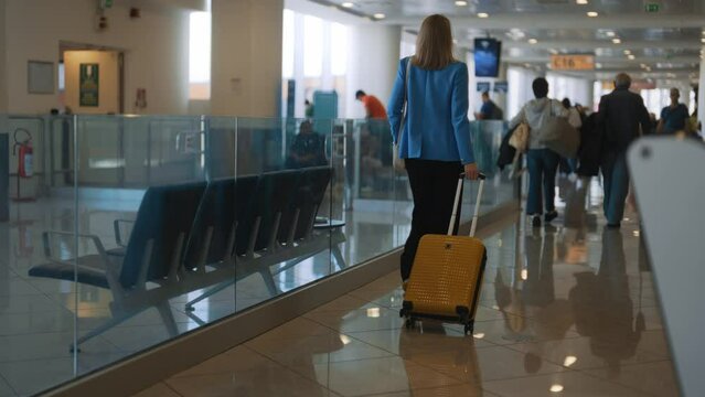 Woman with suitcase walking in airport terminal. Back view.