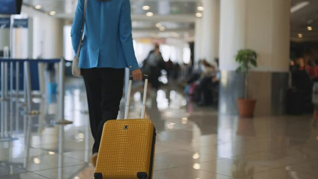 Woman with suitcase walking in airport terminal. Back view.