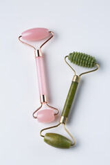 Two cosmetic facial rollers, rose quartz crystal and jade isolated on white background, top view