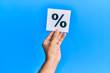Hand of caucasian man holding paper with percentage mark over isolated blue background