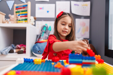 Adorable hispanic girl playing with construction blocks sitting on table at kindergarten