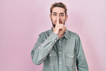 Fototapeta premium Hispanic man with beard standing over pink background asking to be quiet with finger on lips. silence and secret concept.