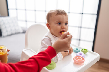 Adorable blond toddler sitting on highchair eating at home