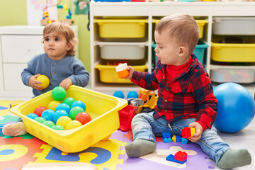 Adorable boys playing with balls and construction blocks sitting on floor at kindergarten