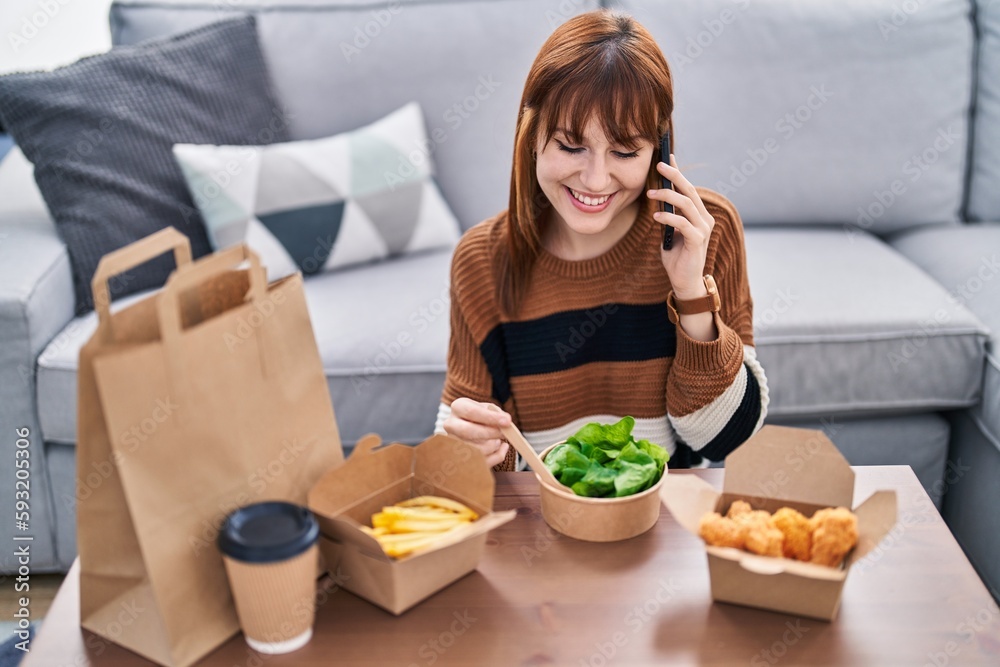 Poster Young woman talking on the smartphone eating take away food at home