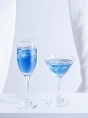 Vertical shot of blue cocktail juice in glasses on a white surface on a white background