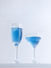 Vertical closeup shot of two glass of blue cocktails on white background.