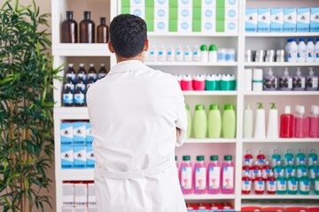 Handsome hispanic man working at pharmacy drugstore standing backwards looking away with crossed arms