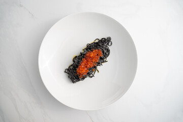 black pasta with red caviar on a white background