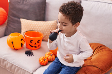 Adorable hispanic boy having halloween party inflating balloon at home