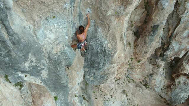 Gerl climber reaches holds, makes effort. Aerial view of Sporty fit woman lead rock climbing on sport route on vertical cliff, outdoors rock climbing, cinematic slow motion rock climbing moments