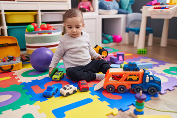 Adorable hispanic boy playing with car toy sitting on floor at kindergarten