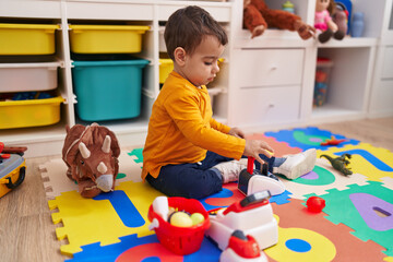 Adorable hispanic boy playing supermarket game sitting on floor at kindergarten