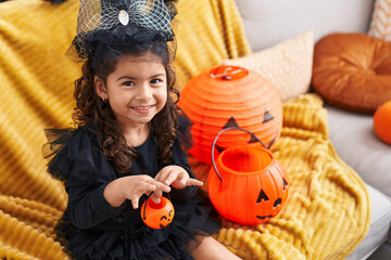 Adorable hispanic girl having halloween party holding pumpkin basket at home