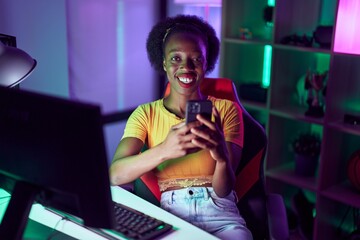 African american woman streamer smiling confident using smartphone at gaming room