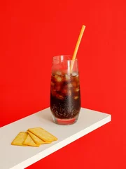 Poster Cold carbonated drink with ice cubes and Cracker Biscuit isolated on red background © Jingluo/Wirestock Creators