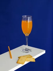 Zelfklevend Fotobehang Yellow Mimosa Cocktail drink and Cracker Biscuit isolated on blue background © Jingluo/Wirestock Creators
