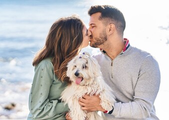 Man and woman holding dog hugging each other kissing at seaside