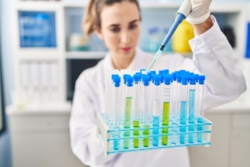 Young woman wearing scientist uniform using pipette working at laboratory