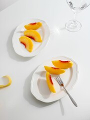 Flat lay of cut peach slices on white plates with a minimalistic table set