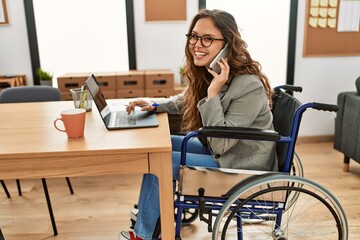 Young beautiful hispanic woman business worker talking on smartphone sitting on wheelchair at office