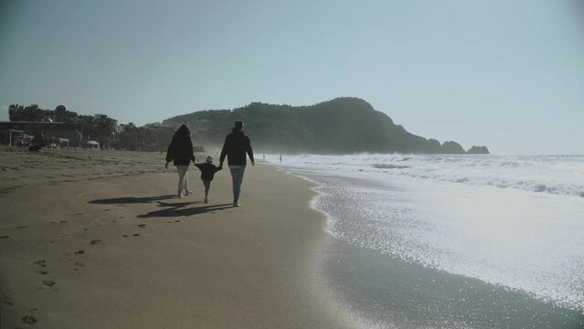 Mom and dad holding hands with the baby and walking on the beach. Slow Motion