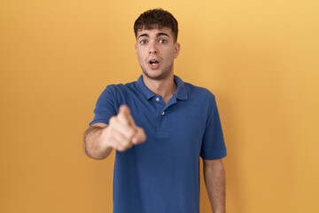 Young hispanic man standing over yellow background pointing displeased and frustrated to the camera, angry and furious with you