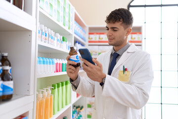 Young hispanic man pharmacist using smartphone holding medication bottle at pharmacy