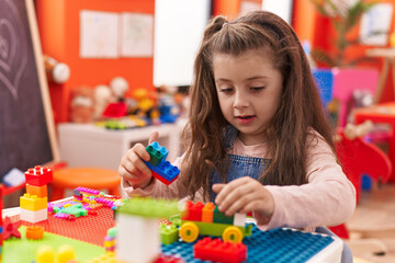 Fototapeta premium Adorable hispanic girl playing with construction blocks sitting on table at kindergarten