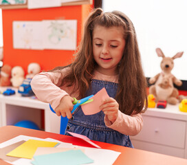 Adorable hispanic girl student smiling confident cutting paper at kindergarten