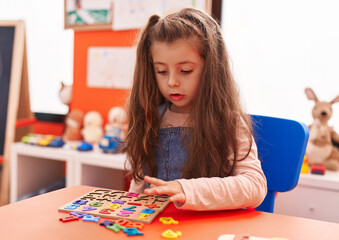 Fototapeta premium Adorable hispanic girl playing with maths puzzle game sitting on table at kindergarten