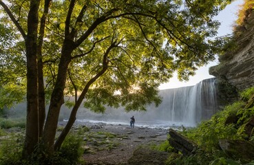 Cute scenery of a couple hugging in front of the Jagala waterfall during a misty sunrise in Estonia