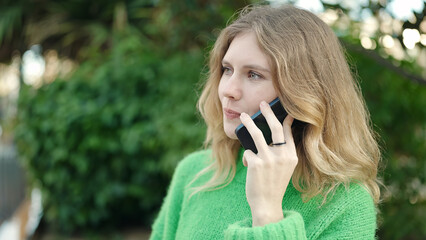 Young blonde woman smiling confident talking on the smartphone at park