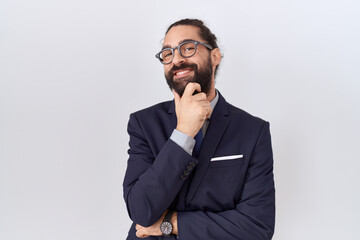 Hispanic man with beard wearing suit and tie looking confident at the camera smiling with crossed arms and hand raised on chin. thinking positive.