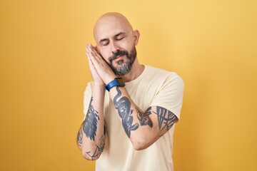 Hispanic man with tattoos standing over yellow background sleeping tired dreaming and posing with hands together while smiling with closed eyes.